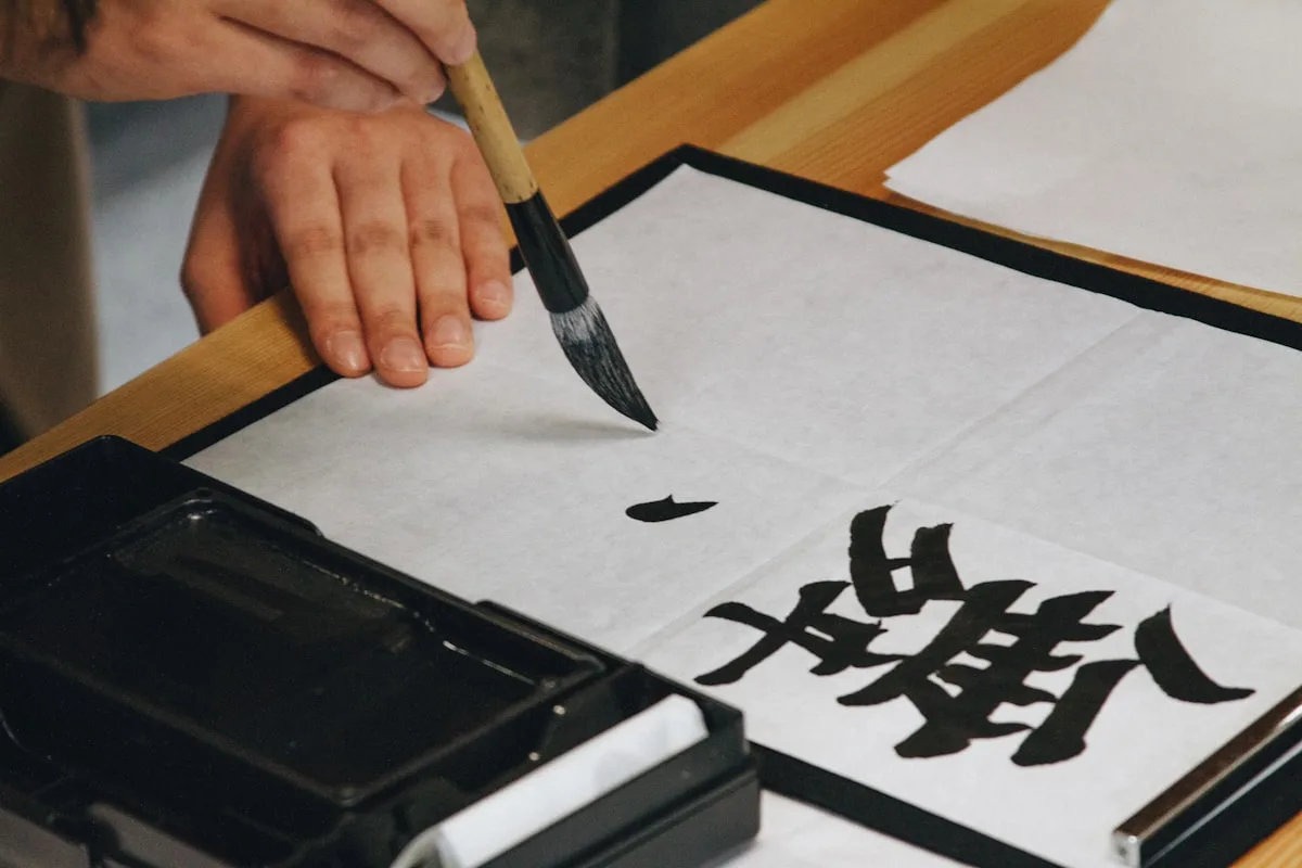 Person writing Chinese calligraphy with a brush on white paper