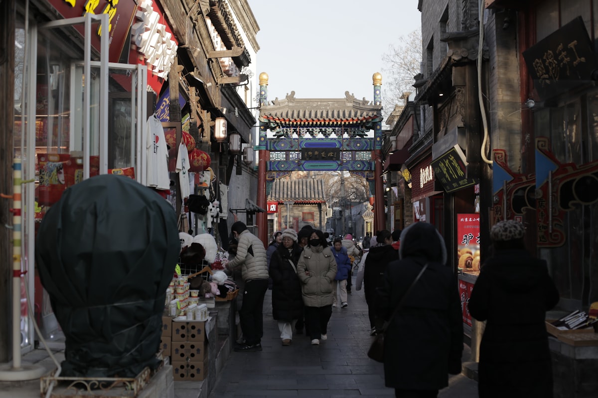 People walking down a narrow street lined with shops in Beijing's hutong neighborhood