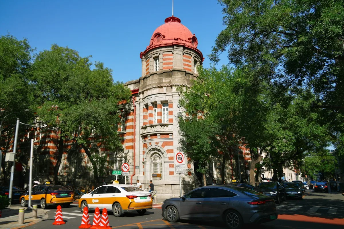 Taxis de Pékin bleus et jaunes passant devant un bâtiment historique à dôme rouge, sur une avenue bordée d'arbres