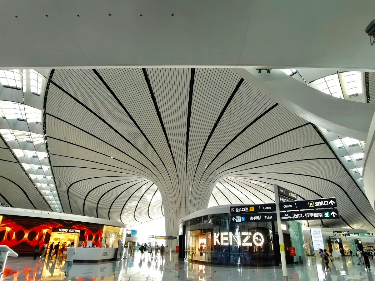 Sala de embarque del aeropuerto de Pekín Daxing con señalización de puertas y tiendas bajo una bóveda blanca