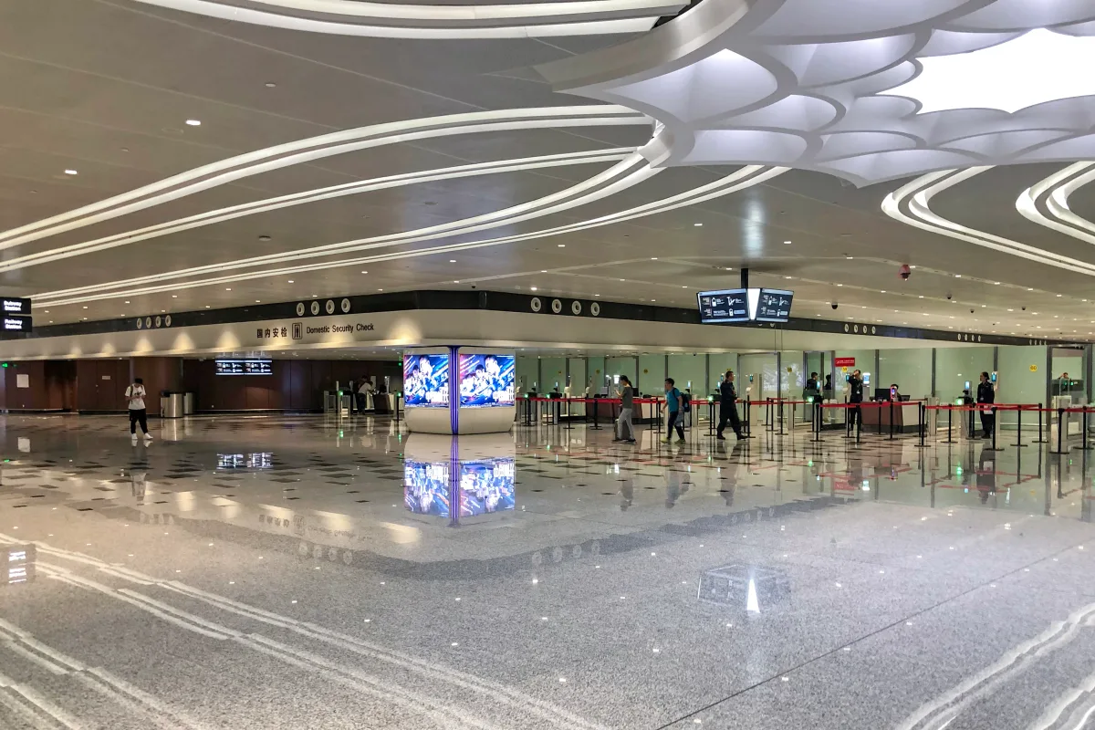 A área de inspeção de segurança doméstica do Aeroporto Internacional de Pequim Daxing, com sinalização bilíngue em chinês e inglês acima das filas de controle (Foto: N509FZ via Wikimedia Commons)