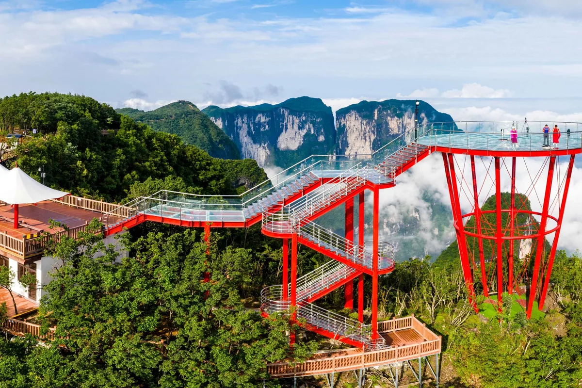 La plataforma de vidrio Ojo del Cielo y una pasarela de vidrio sobre soportes de acero rojos por encima de un mar de nubes, con los pilares de arenisca de Zhangjiajie al fondo