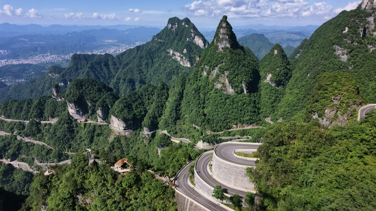 The hairpin road spiralling up Tianmen Mountain's forested slopes, with Zhangjiajie city visible in the distance beyond the peaks