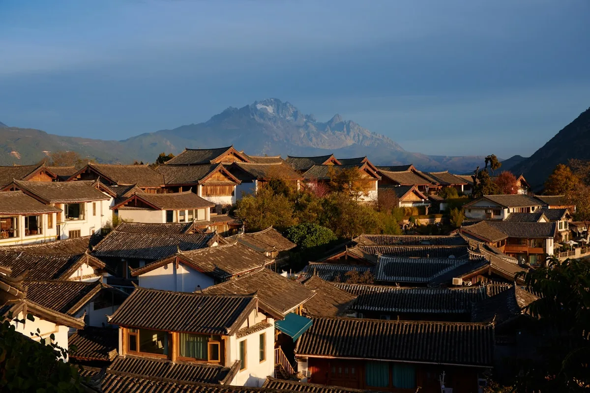 Toits d'un village traditionnel avec montagnes en toile de fond au lever du soleil, Lijiang, Yunnan