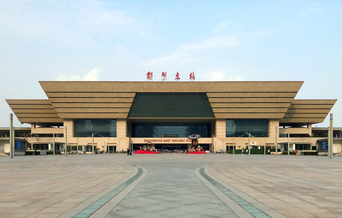 The west facade of Zhengzhou East railway station, a wide layered roof over a glass concourse, seen across an empty paved square (Photo: Windmemories via Wikimedia Commons)