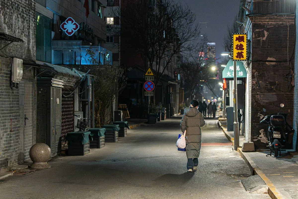 A person in a thick winter coat walking down a street in a Chinese city at night