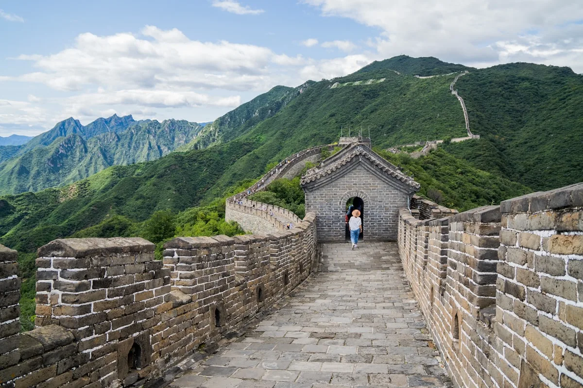 Hikers walking along the restored Mutianyu section of the Great Wall, watchtowers ahead and green ridges behind