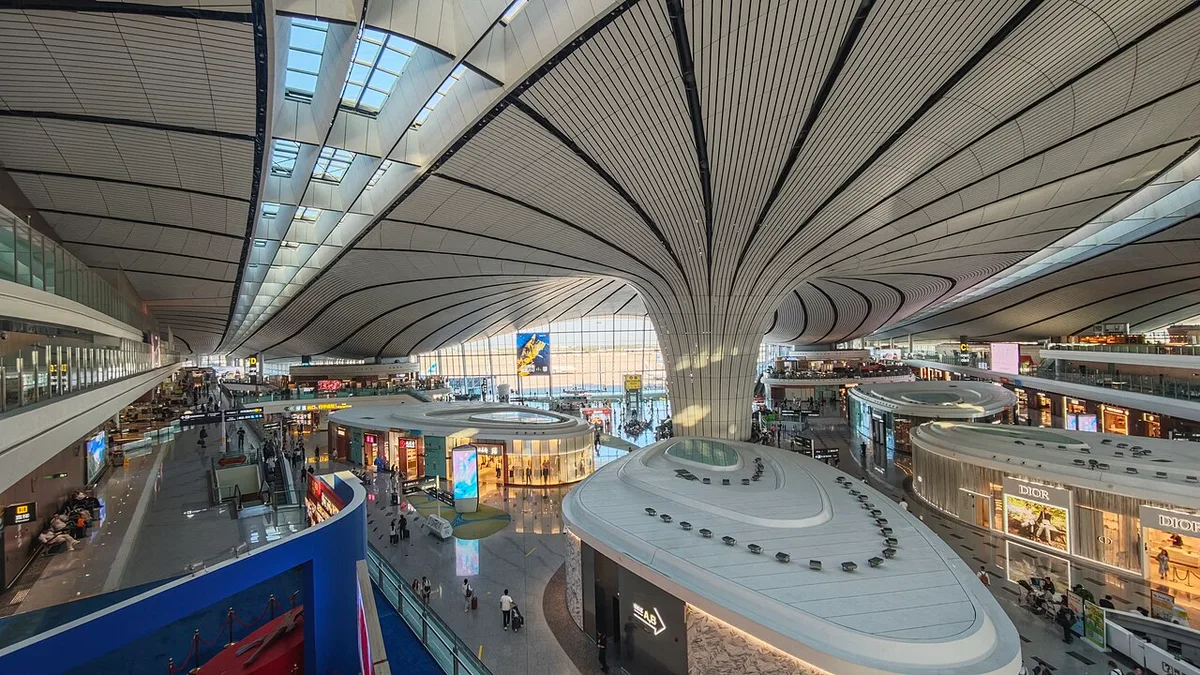 The C-shaped column and ribbed roof of Beijing Daxing airport, with shops and passengers below (Photo: Renek78 via Wikimedia Commons)