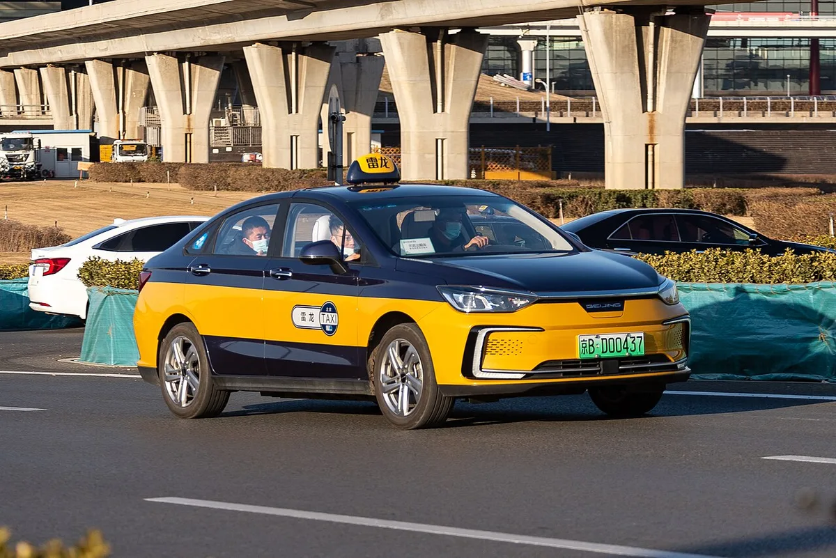A yellow and blue Beijing taxi with a roof sign leaving Capital Airport Terminal 3 (Photo: N509FZ via Wikimedia Commons)
