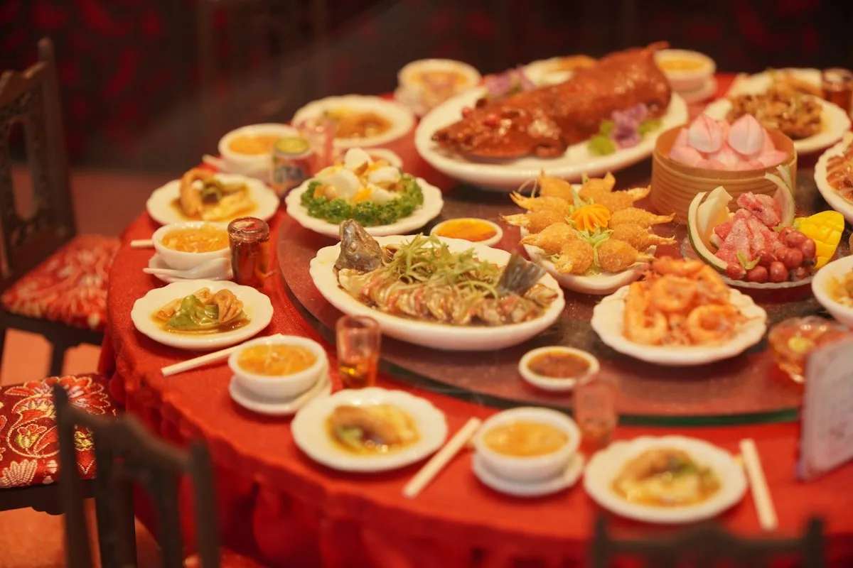 Una mesa redonda de banquete con plato giratorio, cargada con un pato asado entero, pescado al vapor, gambas fritas y cestas de dim sum