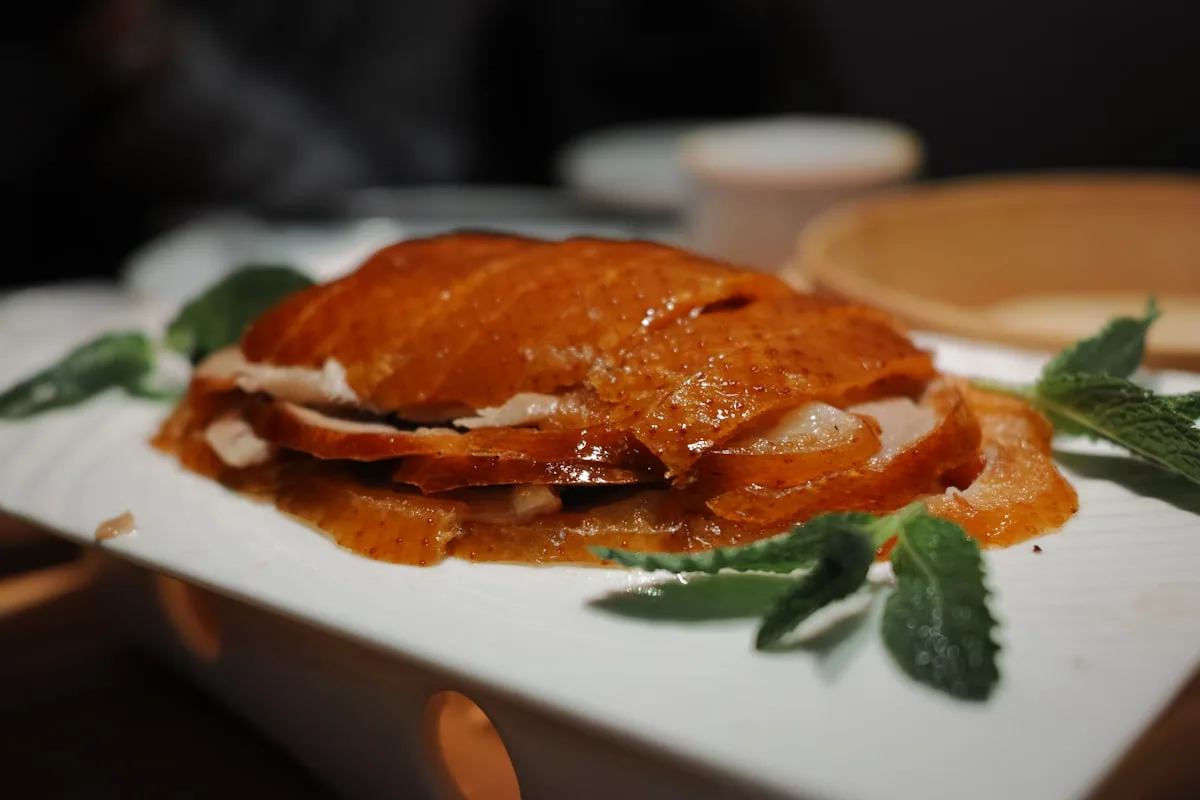 Sliced Peking duck arranged on a plate, a few pieces of scallion and cucumber on the side