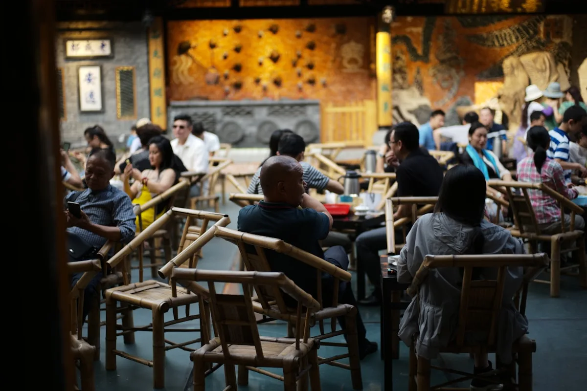 Locals and visitors drinking tea on bamboo chairs in a Chengdu teahouse, lidded gaiwan cups on the tables