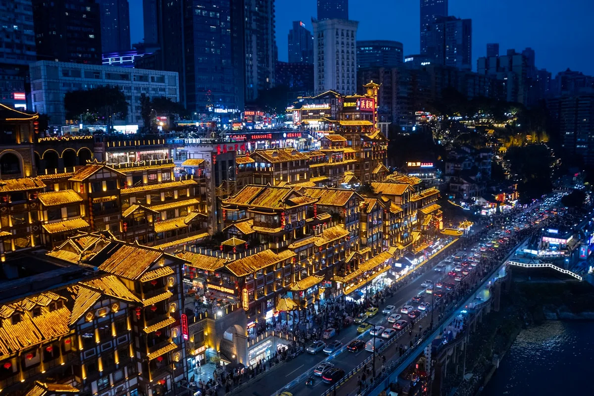 The tiered stilt-house complex of Hongyadong glowing at night, modern towers and busy streets around it