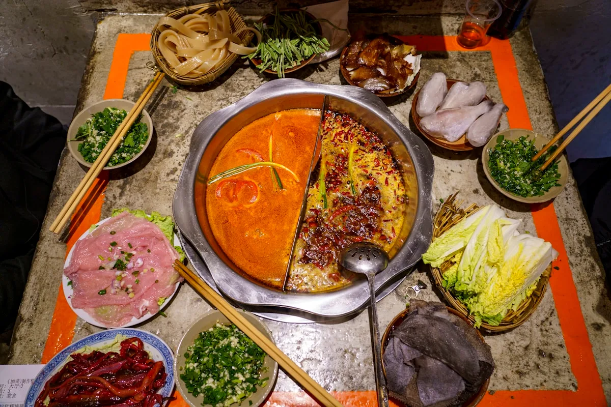 A table of Chongqing hotpot with the pot at the center and plates of meat, tripe, and vegetables around it
