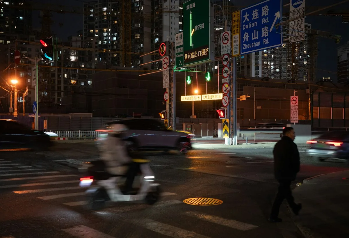 Un carrefour de nuit à Shanghai, avec panneaux routiers éclairés, voitures et un scooter qui traverse
