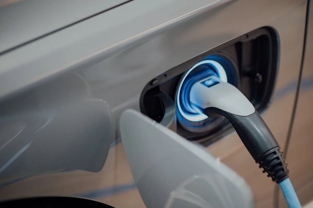 Silver electric car charging, the cable connected to the port with a blue light