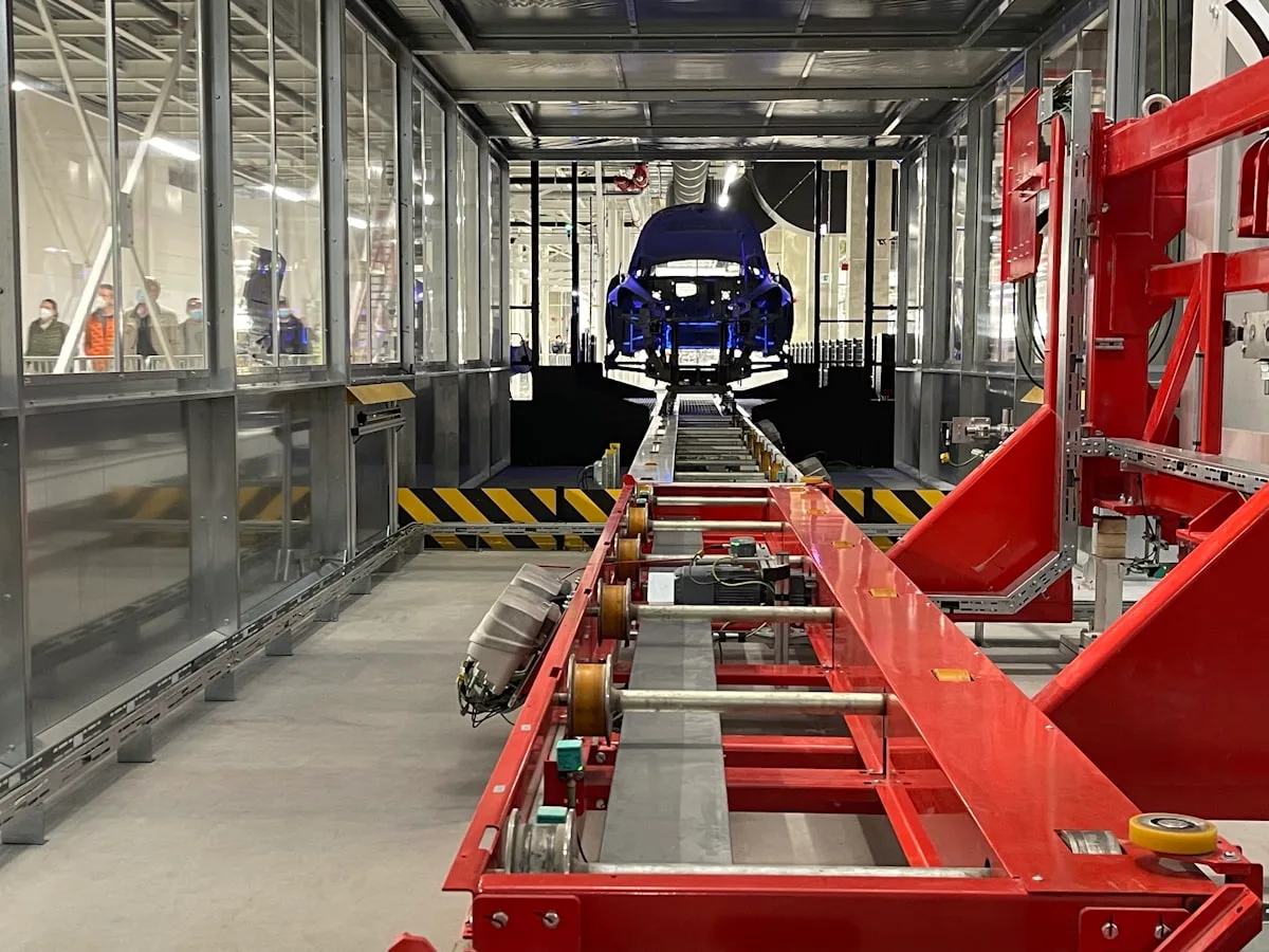 A Chinese EV factory assembly line viewed from a glass visitors' gallery, car bodies moving along the conveyor