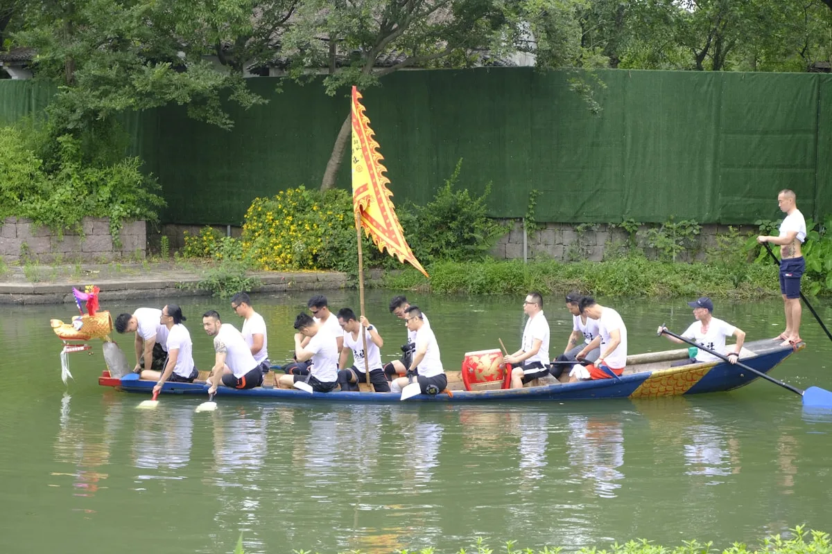 Rowers in white shirts paddling a decorated dragon boat along a canal in a Chinese water town