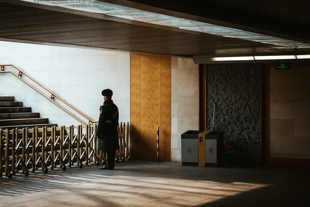 A uniformed security guard standing in an indoor corridor of a Chinese public building