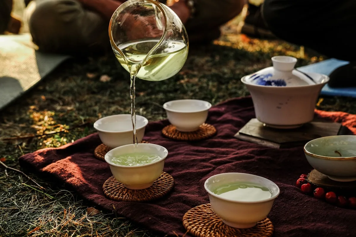 A traditional Chinese tea setup outdoors, with tea being poured from a glass pitcher into a small cup on a wooden tray