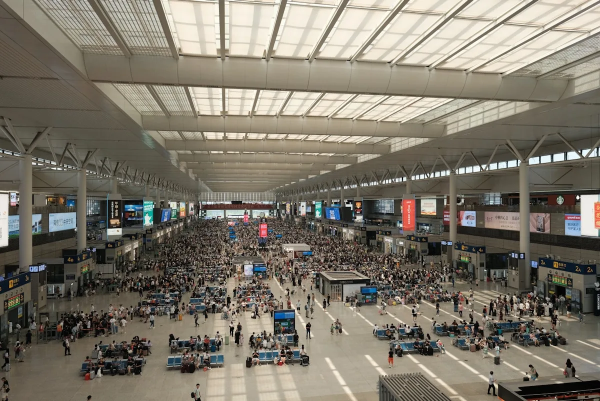 The crowded waiting hall of a Chinese high-speed rail station, hundreds of passengers flowing through a modern concourse