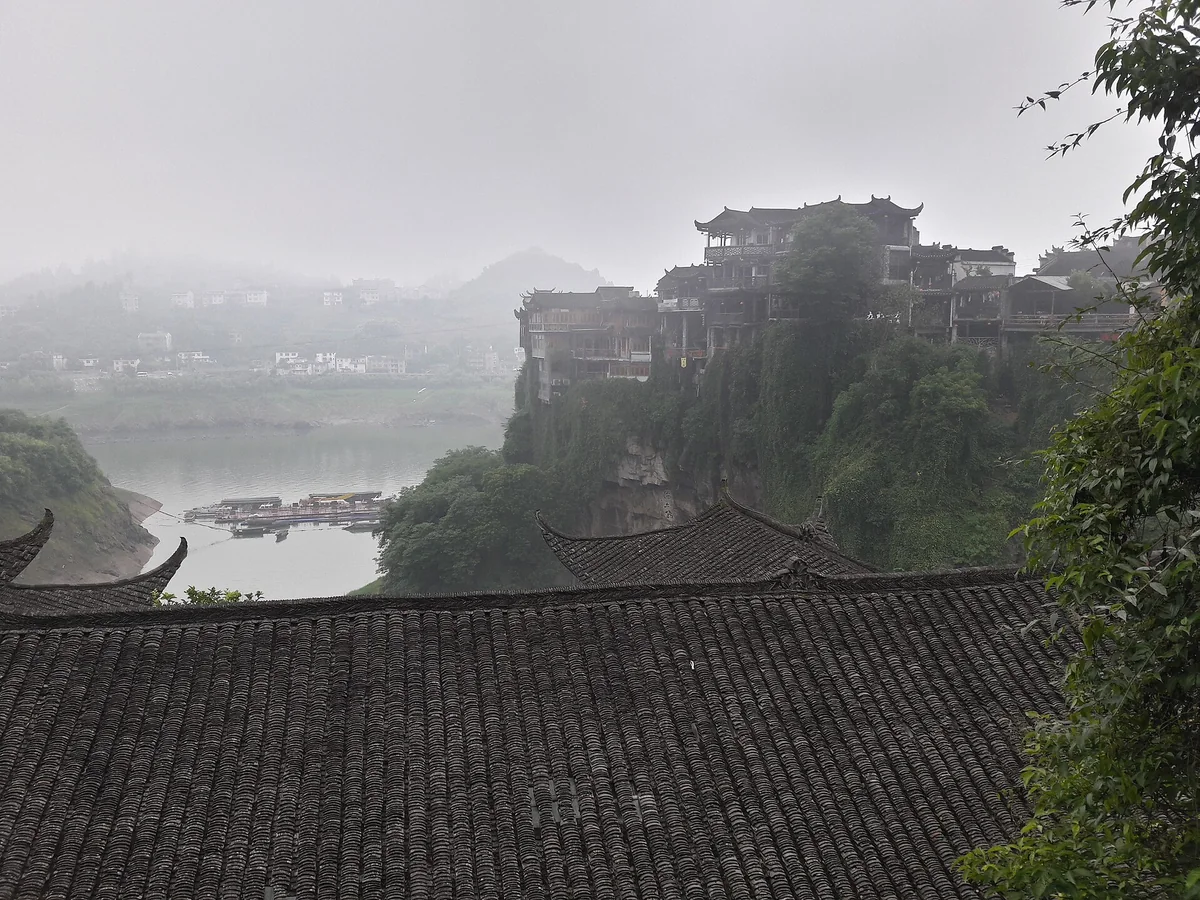 Brume matinale dans le gouffre de Furong, avec les maisons sur pilotis du rebord de falaise émergeant au-dessus de la rivière Youshui (Photo : Popolon via Wikimedia Commons)