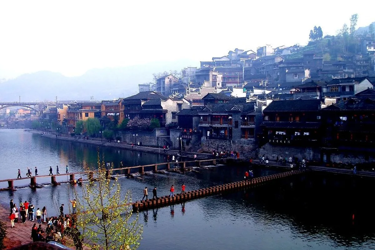La rivière Tuo à Fenghuang, avec des passants sur les pierres de gué au premier plan et des maisons sur pilotis alignées sur la rive opposée sous la ville (Photo : Yu Hui via Wikimedia Commons)