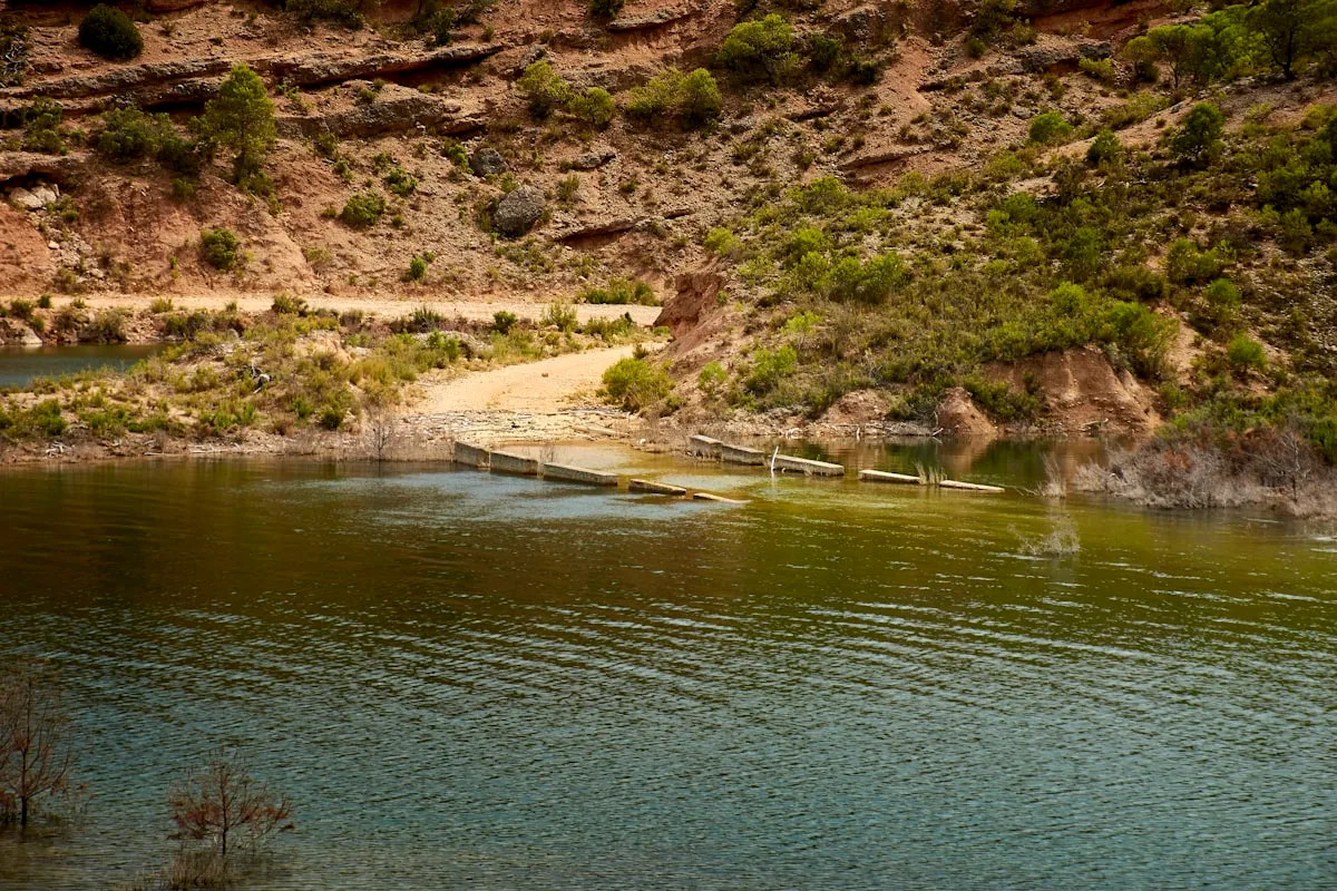 Un pont en bois traverse un lac paisible entouré de collines.
