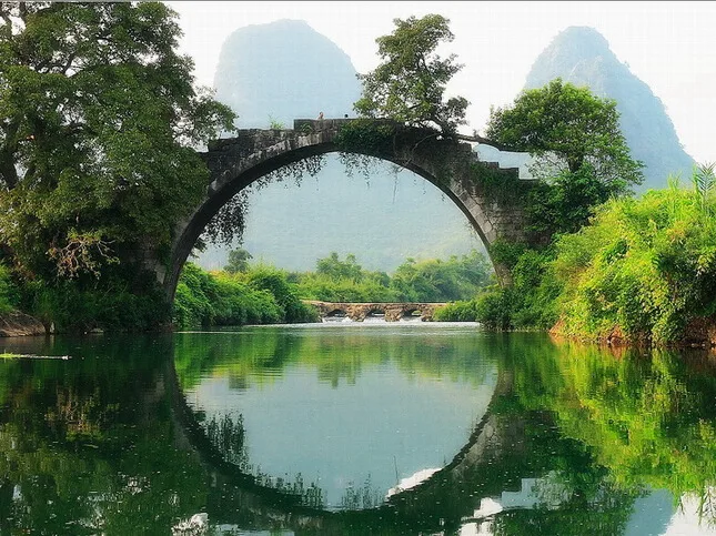 Fuli Bridge: a 500-year-old Ming Dynasty stone arch bridge forming a perfect circle with its reflection in the still Yulong River