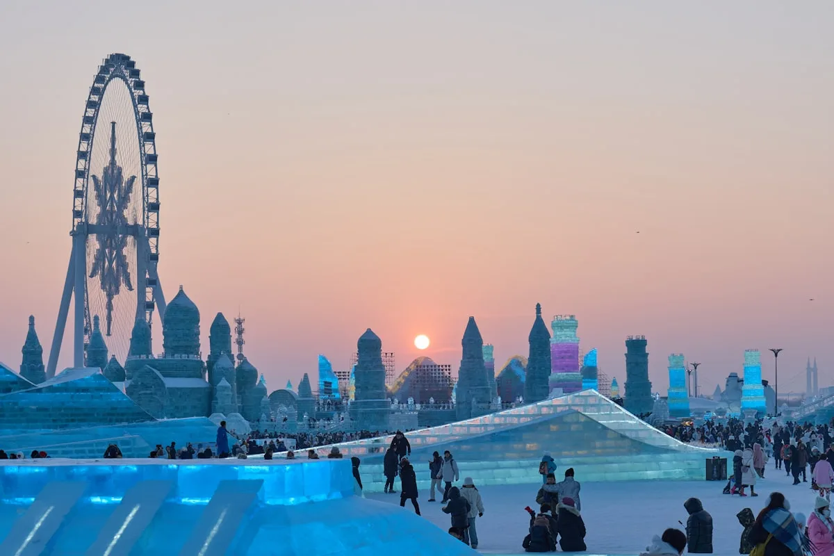 Harbin Ice and Snow World at sunset, ice towers and a large Ferris wheel rising above snowy walkways