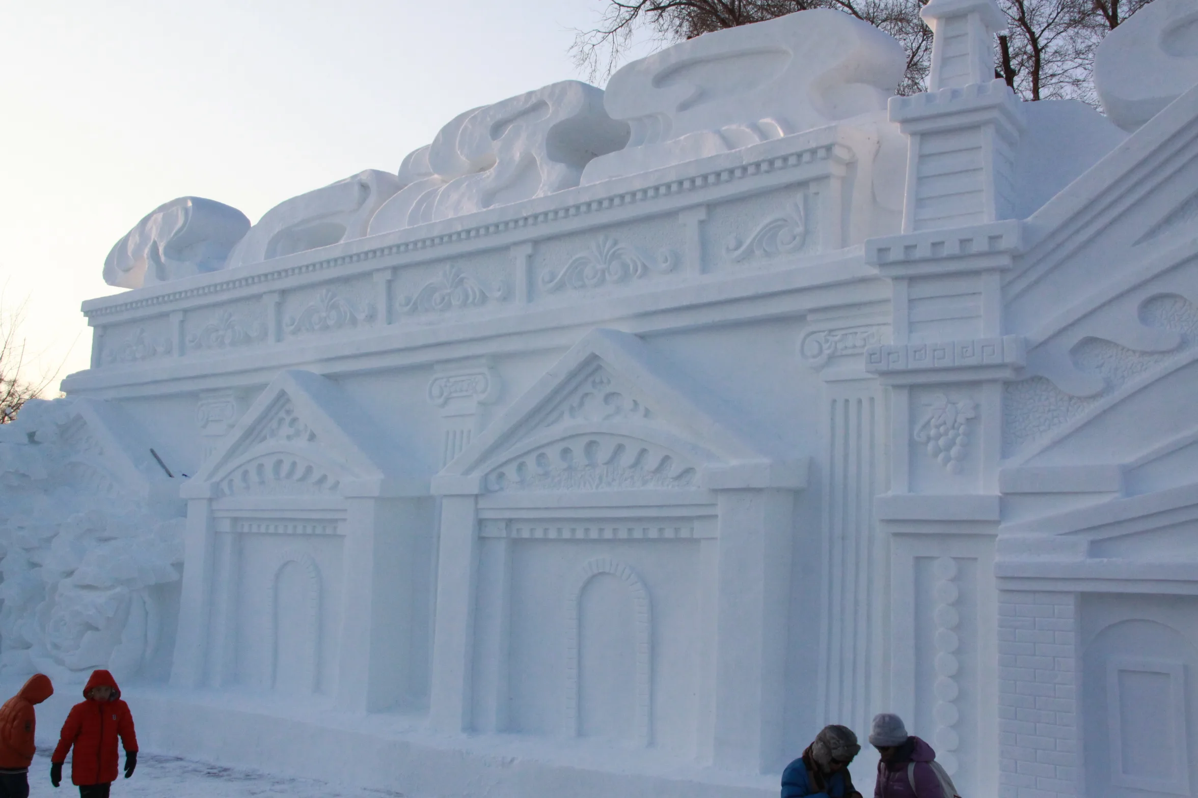 Visitors walking past a finely carved snow sculpture of a classical building with columns and relief details at the Sun Island Snow Sculpture Expo in Harbin (Photo: Caliva via Wikimedia Commons)