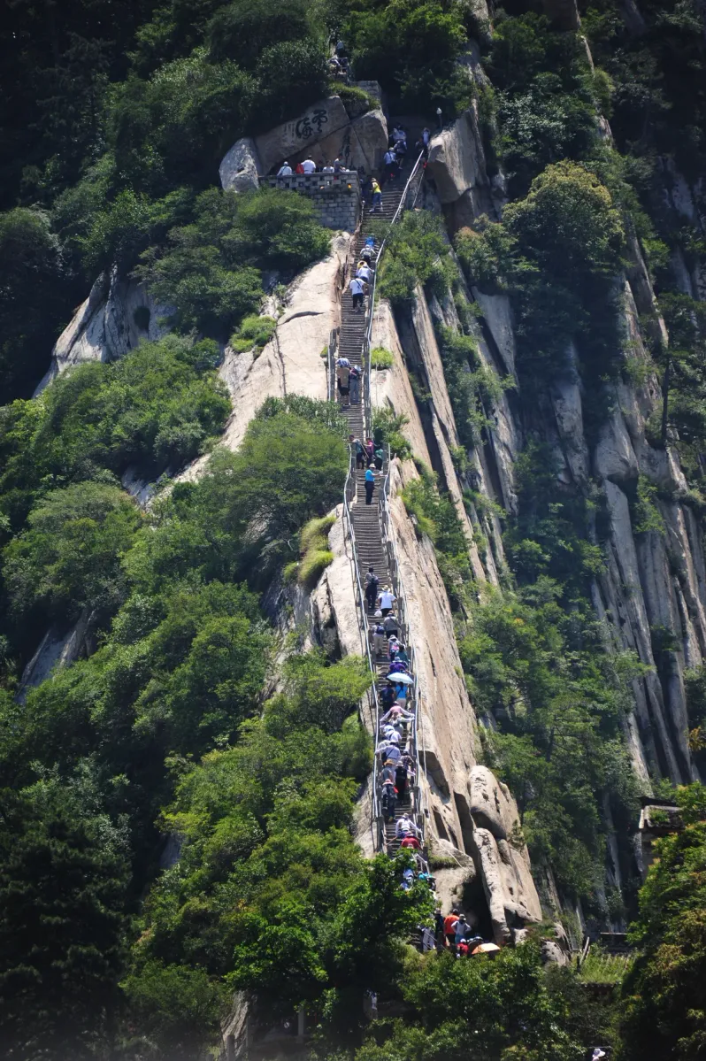 Escaliers de pierre et chaînes de maintien sur une paroi de granit à Huashan, avec des marcheurs échelonnés le long de l'escalier (Photo: chensiyuan via Wikimedia Commons)