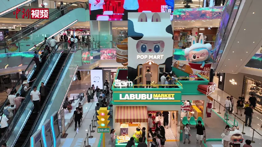Le pop-up Labubu Market dans un centre commercial de Pékin en juin 2025, avec une tête de Labubu géante au-dessus de l'entrée et la foule sur les escalators autour (Photo: 中国新闻社 via Wikimedia Commons)