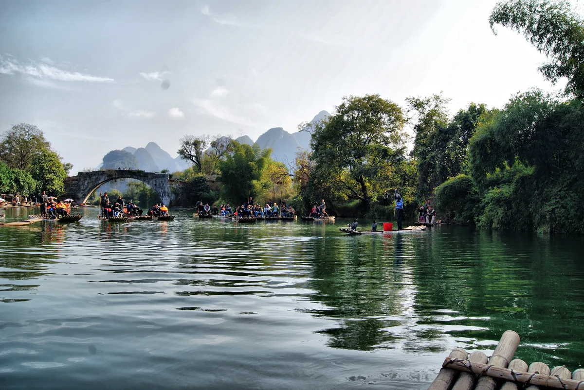 A hand-poled bamboo raft on the Yulong River passing under a stone arch bridge near Yangshuo (Photo: HALUK COMERTEL via Wikimedia Commons)