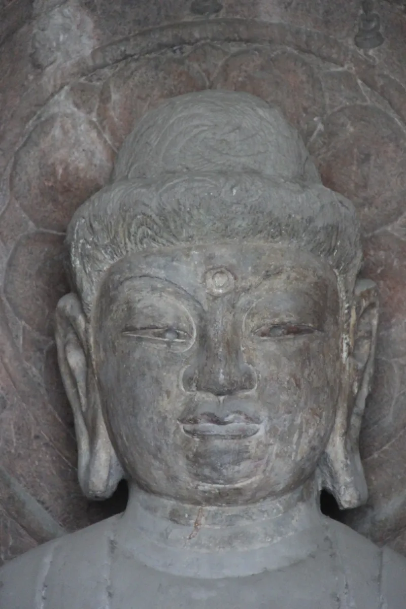 Uma cabeça de Buda em alto-relevo nas grutas de Longmen, com os olhos semicerrados e o nimbo esculpido atrás marcado pelo tempo (Photo: Gary Todd via Wikimedia Commons)