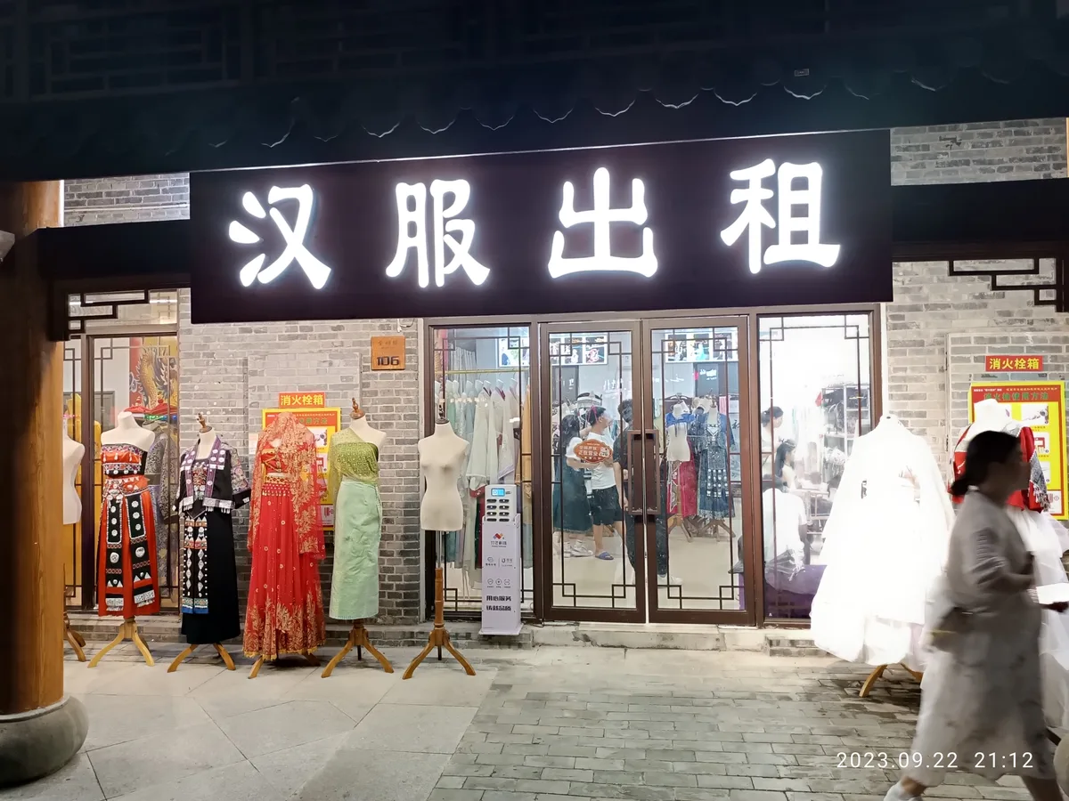 Une boutique de location de hanfu la nuit, son entrée bordée de mannequins habillés sous une enseigne lumineuse annonçant la location de hanfu, avec des portants de costumes visibles derrière la vitre (Photo: Nan Ning Huang Sokaz 12 via Wikimedia Commons)