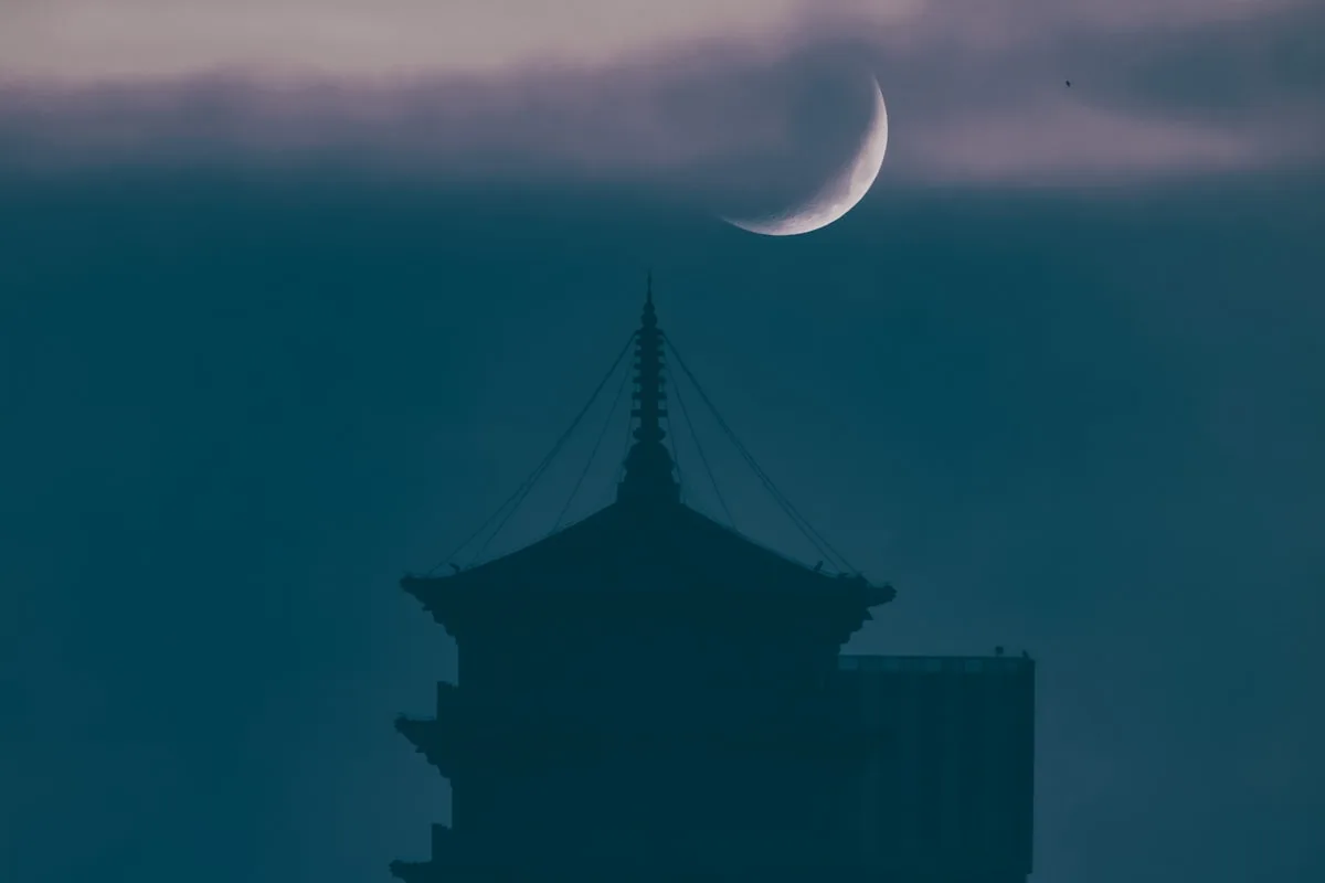 A Chinese pagoda silhouetted against a crescent moon and dusk clouds, the classic moon-viewing scene of Mid-Autumn