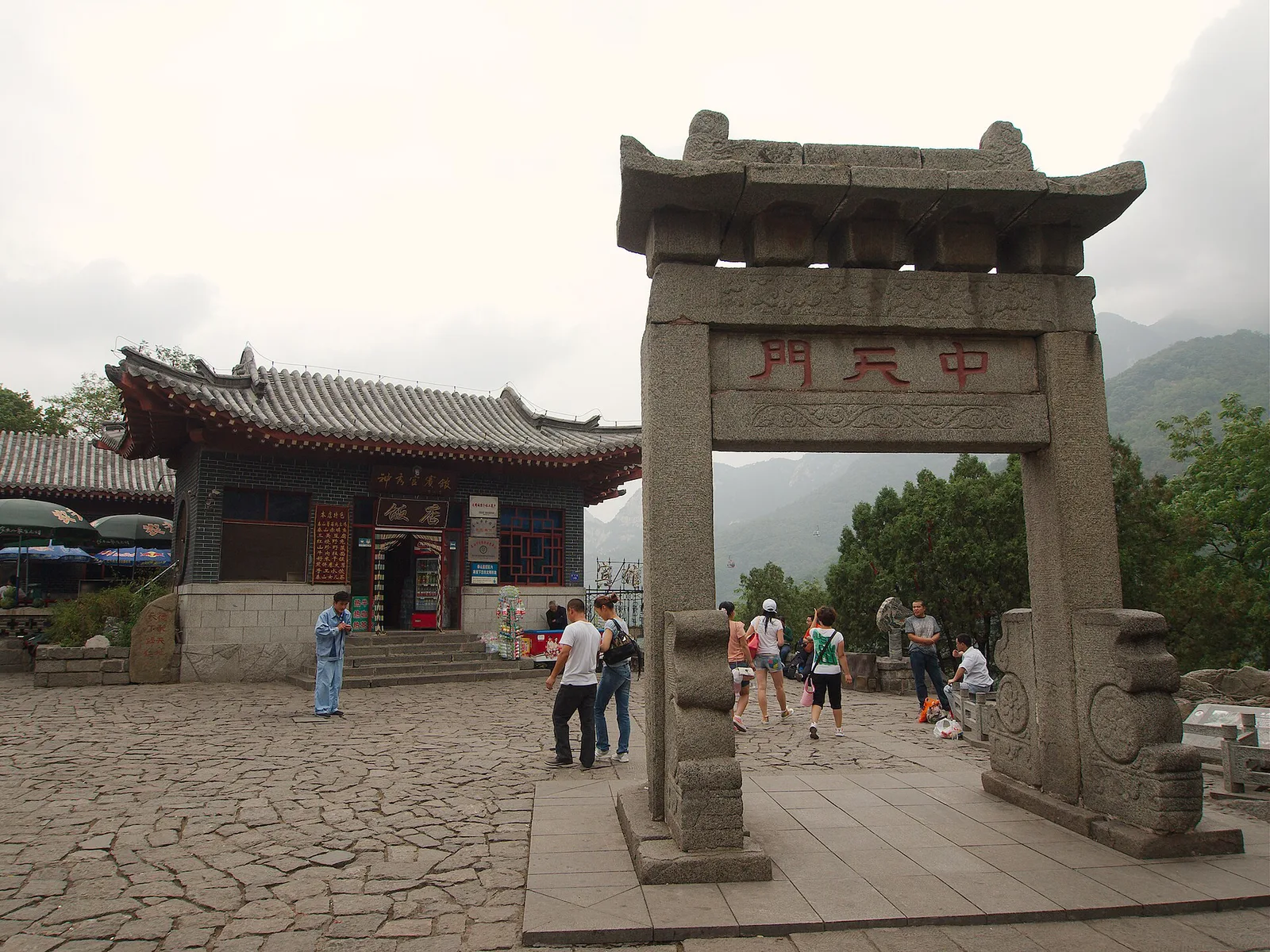 The stone archway at Zhongtianmen on Mount Tai, its plaque reading Halfway Gate to Heaven, with shops, a paved terrace and the ridge behind
