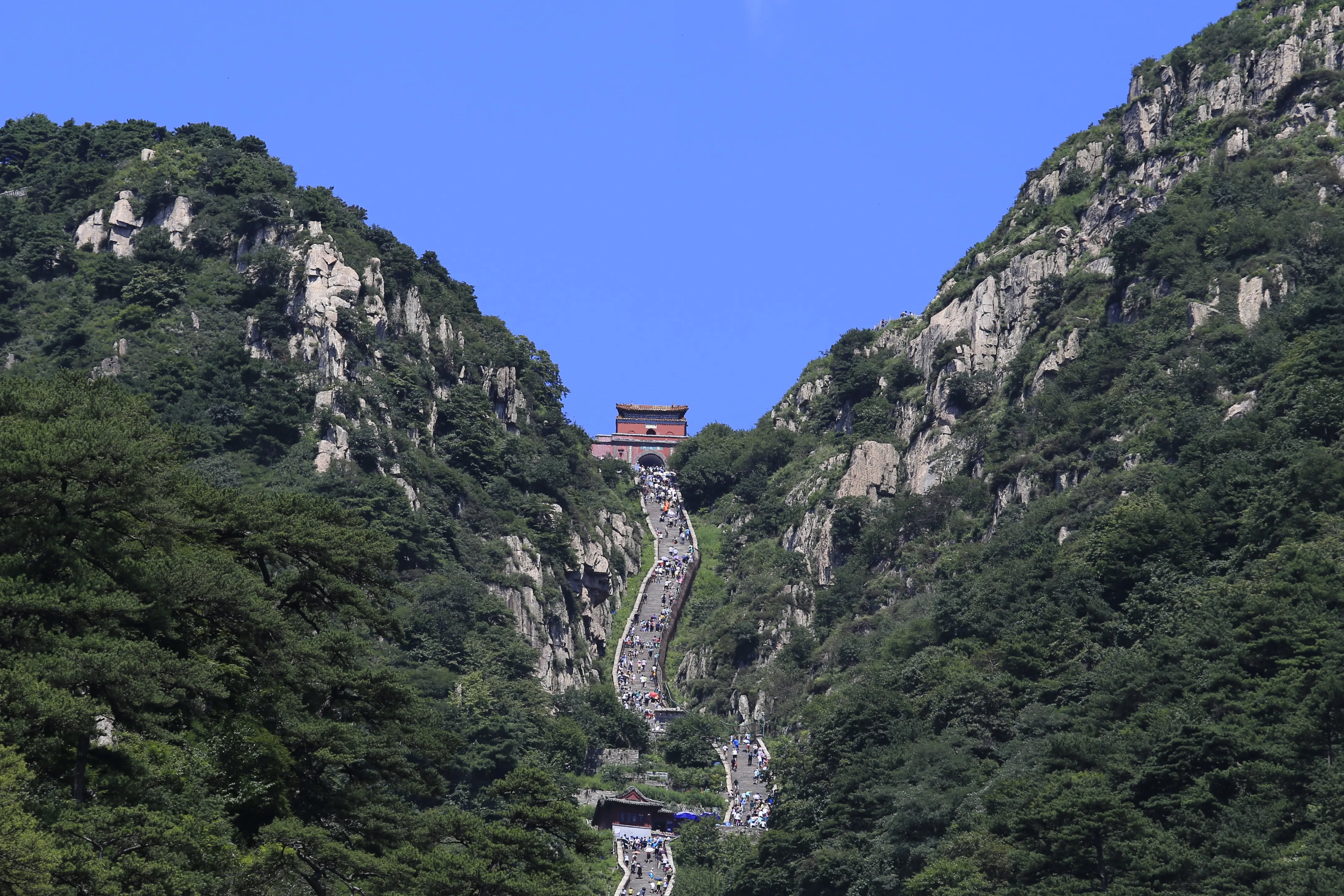 Caminantes repartidos a lo largo de la empinada escalera de piedra de las Dieciocho Curvas en el monte Tai, con la puerta roja de Nantianmen en lo alto del barranco (Foto: Zhangzhugang vía Wikimedia Commons)