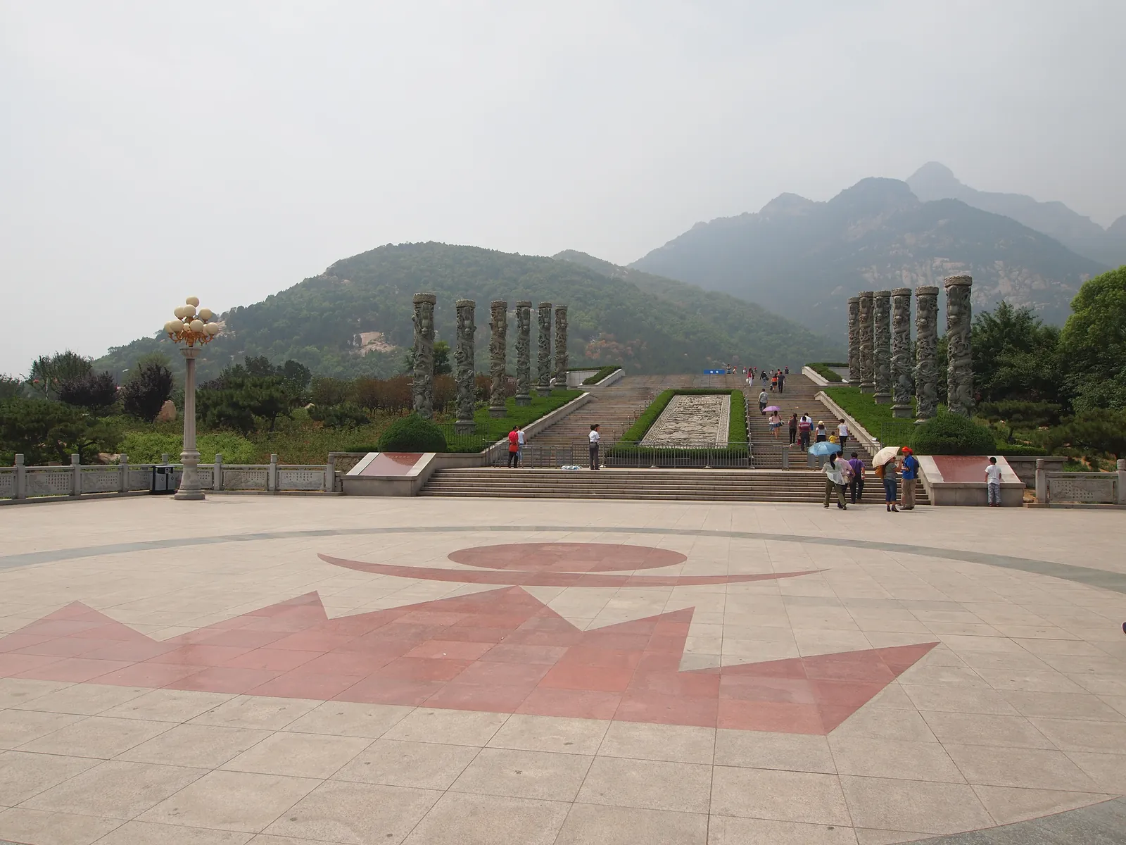 La place pavée de Tianwaicun au pied du mont Tai, avec ses colonnes de pierre, ses marches et la crête de la montagne en arrière-plan, d'où part la navette vers Zhongtianmen (Photo : rheins via Wikimedia Commons)