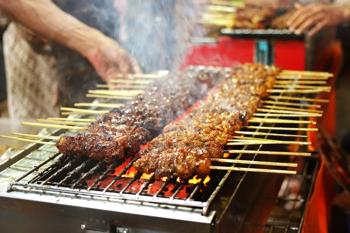 Meat skewers grilling over a charcoal brazier at a Chinese street food stall with smoke rising