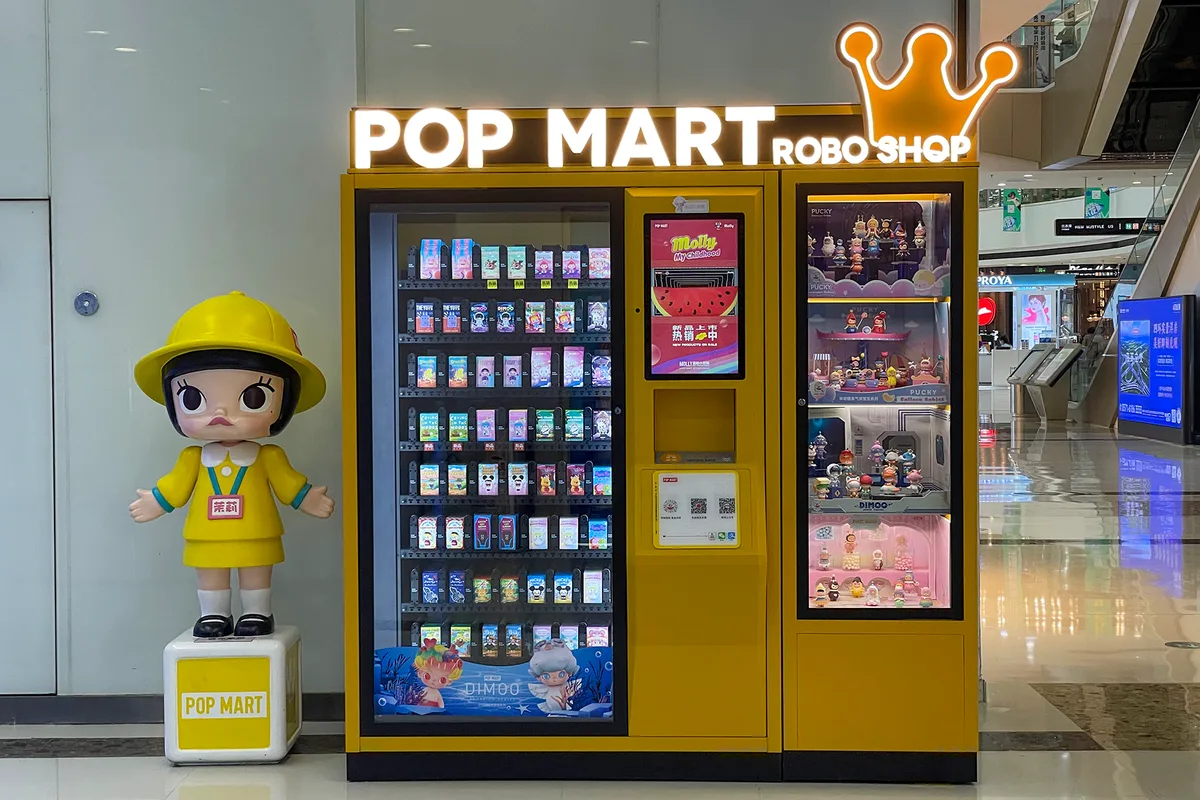 Un distributeur Pop Mart Robo Shop à côté d'une statue Molly dans un centre commercial de Zhengzhou, avec des rangées de blind box visibles derrière la vitre (Photo: Windmemories via Wikimedia Commons)