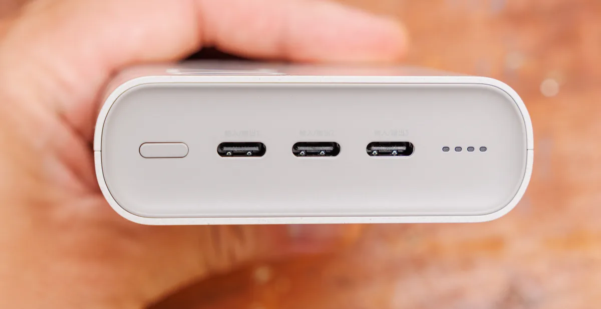 Um power bank branco segurado em uma mão, com três portas USB-C rotuladas em chinês e uma fileira de luzes indicadoras de carga na lateral (Foto: Dinkun Chen via Wikimedia Commons)