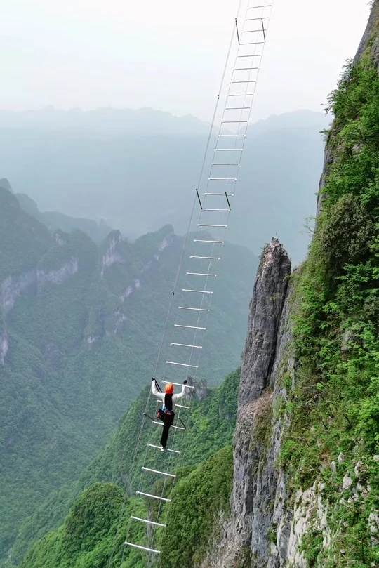 Un escalador con casco a media altura de la Escalera del Cielo Lingyun, con el valle boscoso muy abajo