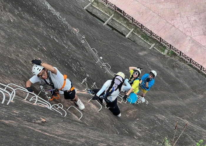 Cuatro escaladores con casco y arnés asegurados al cable de seguridad en la losa de roca de la vía ferrata