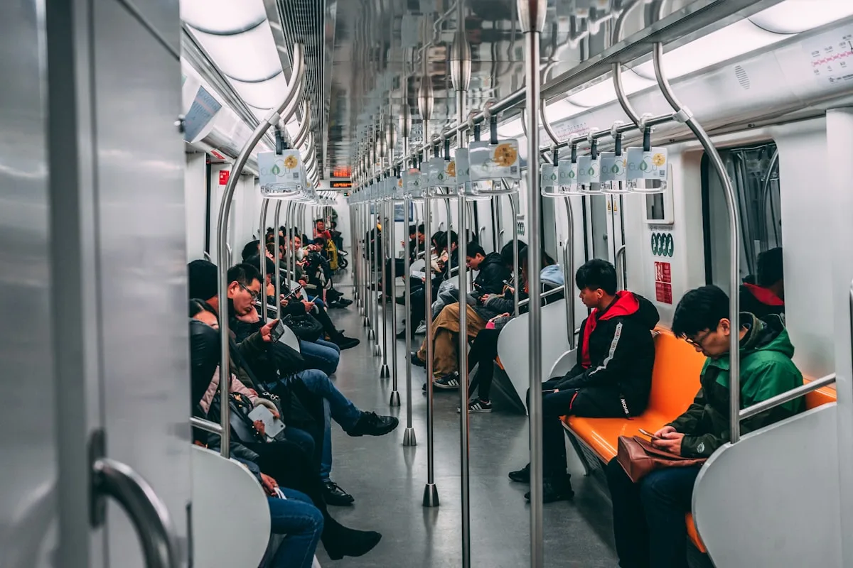 Passengers sitting on orange seats inside a Chinese metro train carriage, several checking their phones as the train runs between stations