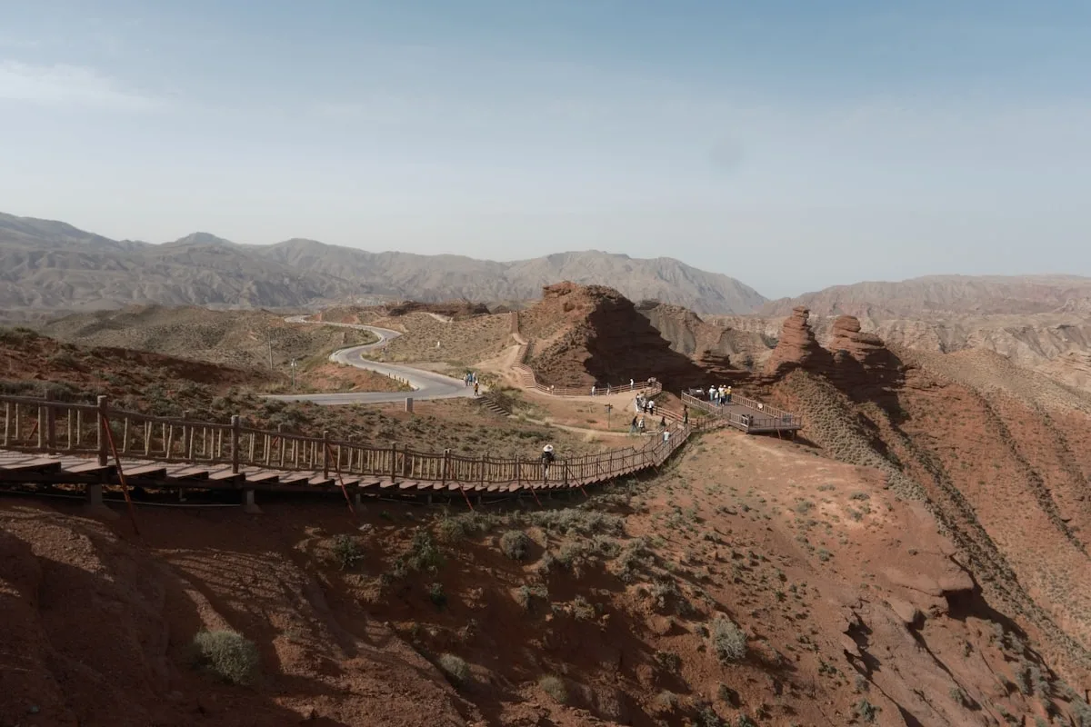 Rainbow-hued sandstone ridges of Zhangye Danxia with a boardwalk winding across, visitors tiny against the scale of the colored hills