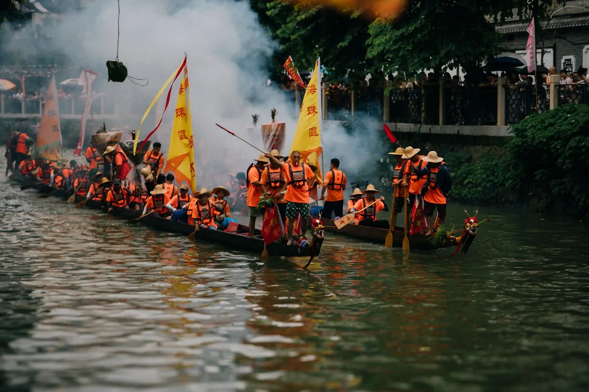 Dragon boat paddlers in orange life vests racing on the Pearl River in Guangzhou, a yellow district banner flying from the lead boat