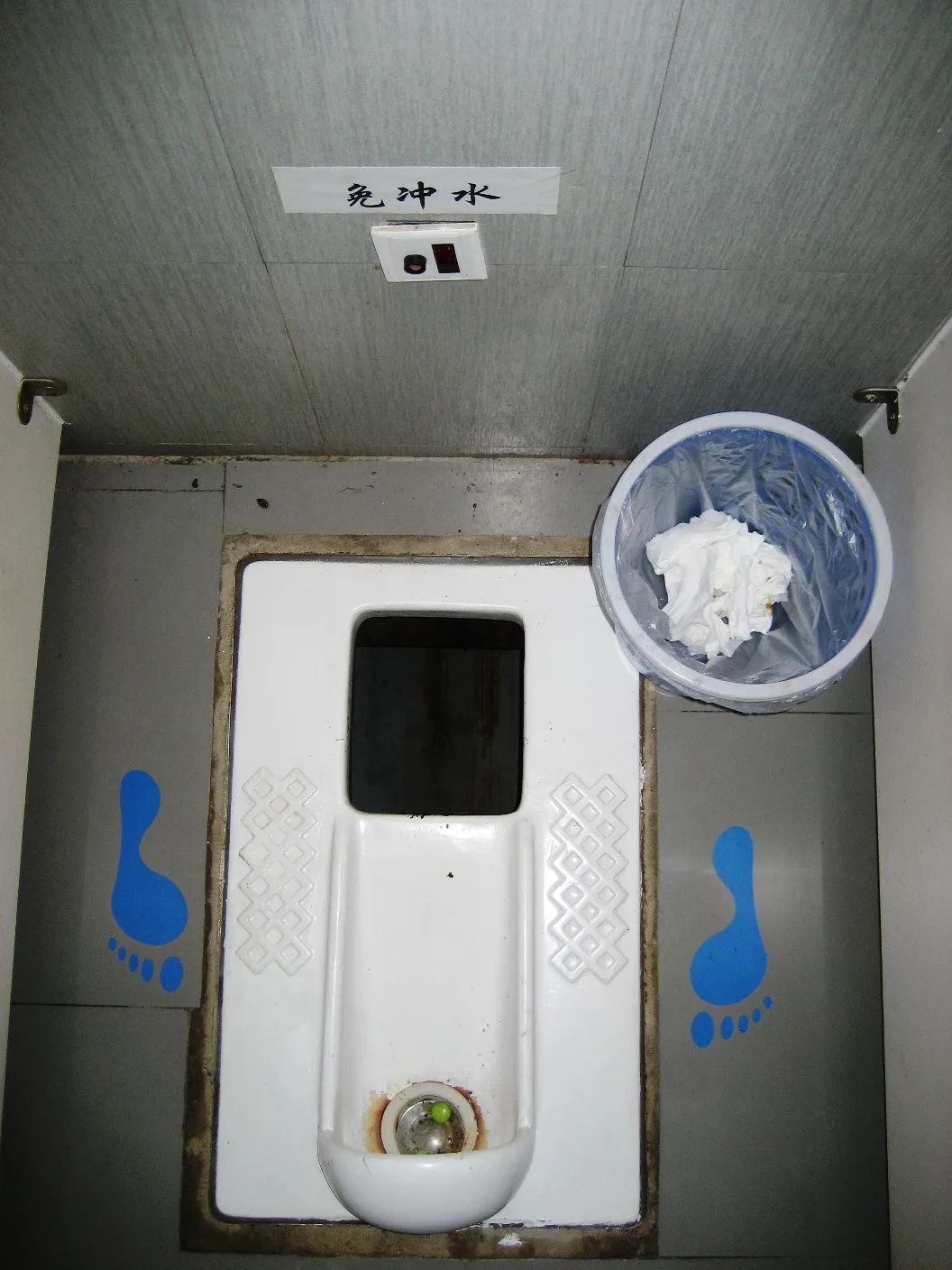 A squat pan with painted footprint guides on either side and a no-flush notice on the wall (Photo: SuSanA Secretariat via Wikimedia Commons)