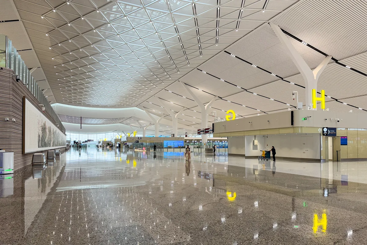 El vestíbulo de salidas de la terminal 5 del aeropuerto internacional de Xi'an Xianyang, un suelo reflectante y largo bajo un techo facetado, con el pabellón de tejado dorado del museo del aeropuerto visible en el lado izquierdo (Photo: Windmemories via Wikimedia Commons)